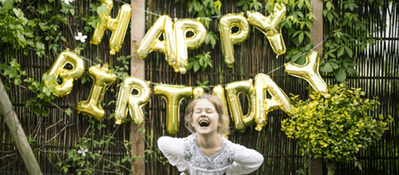 Une fille joyeuse qui célèbre un anniversaire, derrière elle se trouve des ballons avec écrit happy birthday